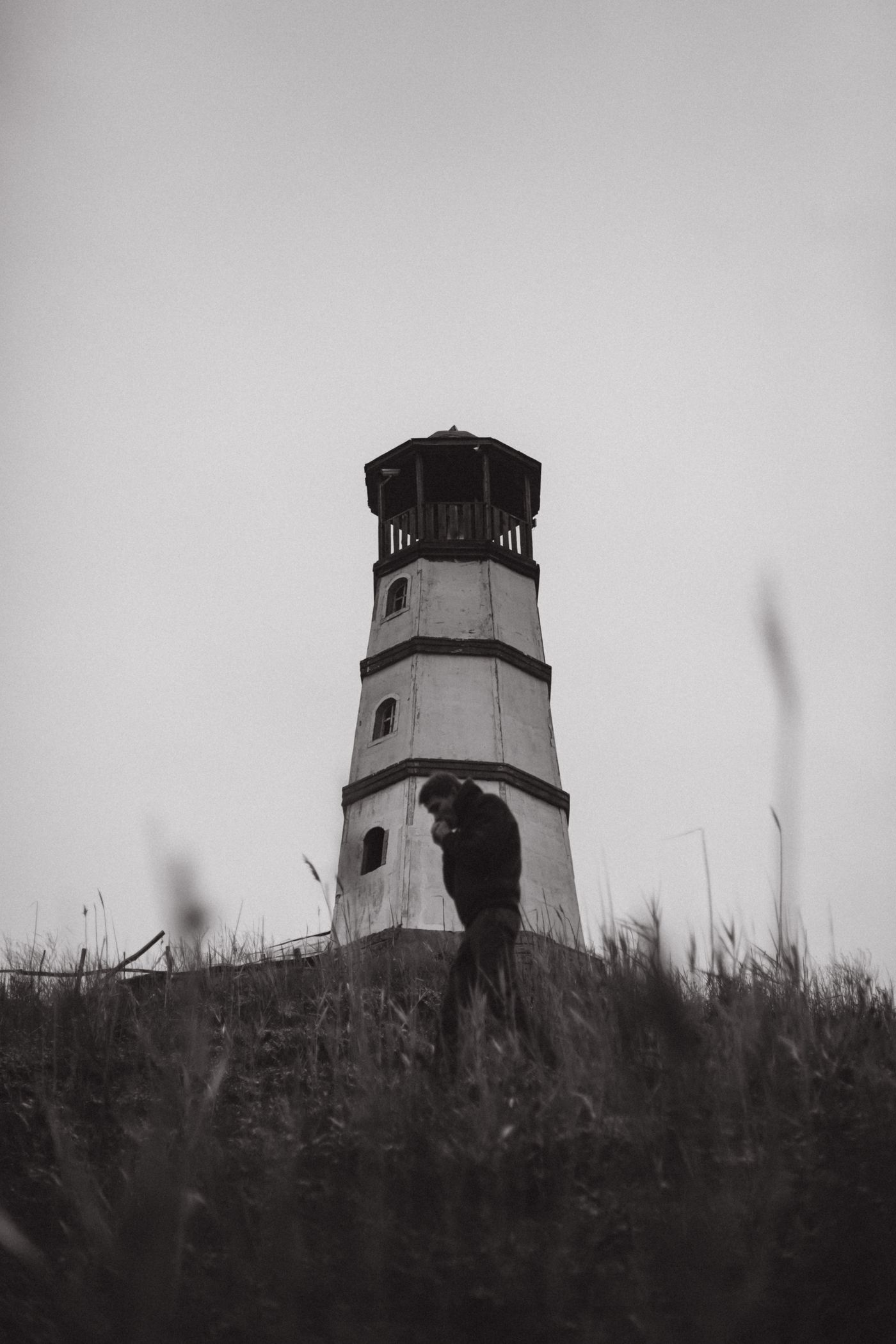 A lone person walking through a misty field near a lighthouse