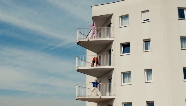 Three people stretching on separate balconies of a white apartment building