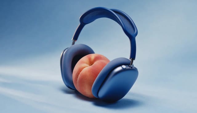 Blue over-ear headphones holding a peach against a blue studio background